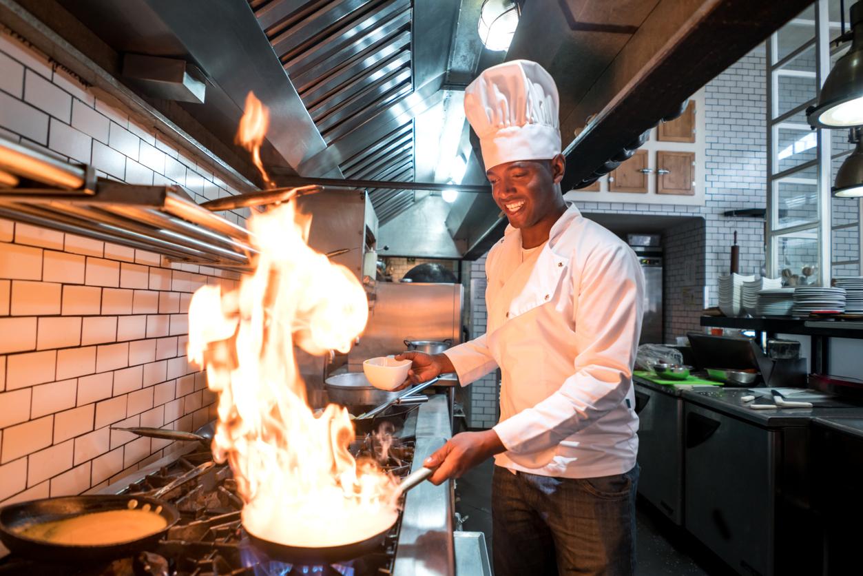 A chef prepares a meal under the exhaust hood of a commercial kitchen.