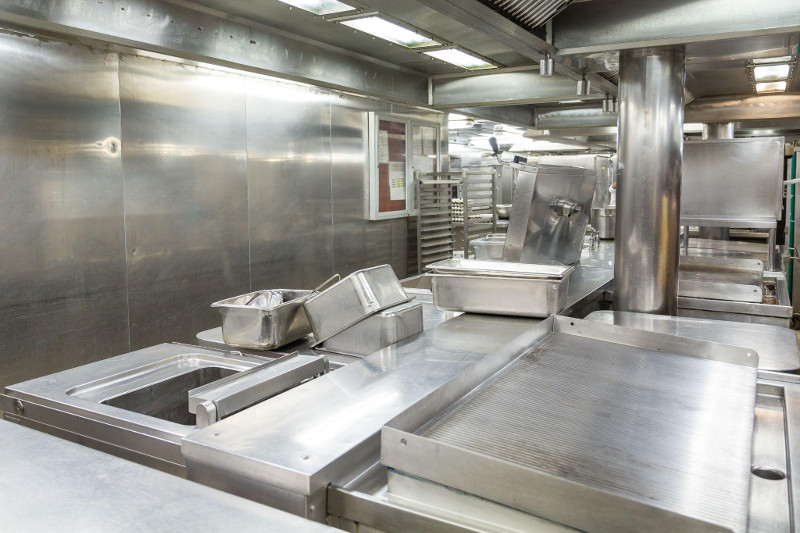 The clean, bright interior of a commercial kitchen with stainless steel wall panels is shown.